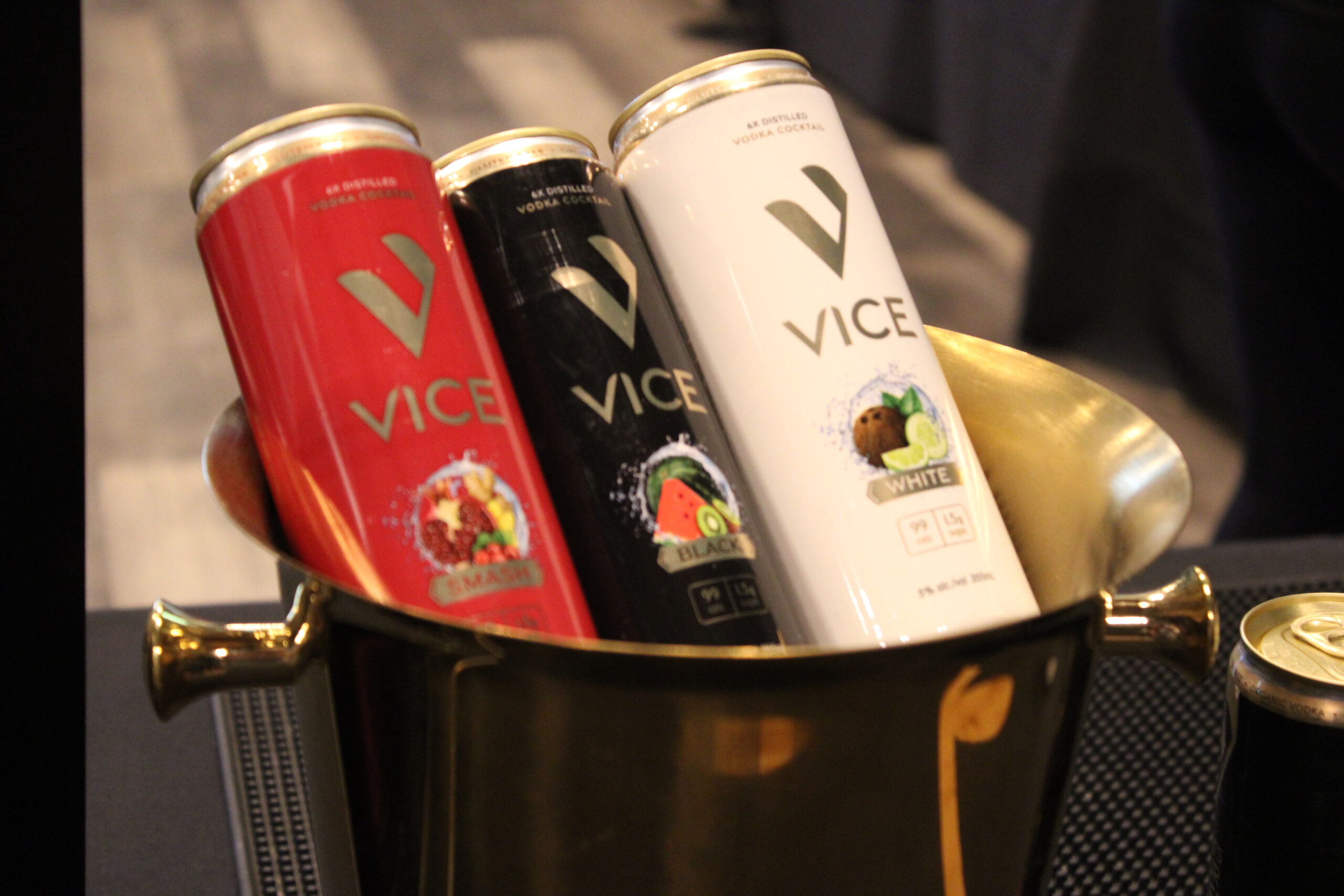 Three Vice vodka cocktail cans in red, black, and white colors placed inside a gold ice bucket.