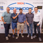 Five men smile and pose together in front of a large "DIXONLICIOUS" event backdrop featuring sponsor logos.