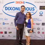A man and a woman pose and smile in front of a "DIXONLICIOUS" event backdrop featuring various sponsor logos.