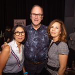 Three people pose together at a social event, smiling at the camera in a well-lit indoor setting.