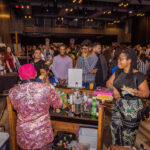 A bartender in a sparkly pink jacket serves drinks to a crowd at a lively event, with people watching and taking photos.