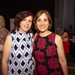 Two smiling women pose together at an event, wearing patterned dresses.