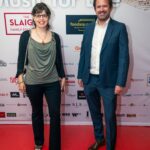 A smiling man and woman pose on the red carpet at the "Music for Life" event, standing in front of a branded backdrop featuring sponsor logos.