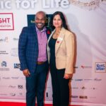 A man and a woman pose together on the red carpet at the "Music for Life" event, standing in front of a backdrop featuring sponsor logos and musical notes.